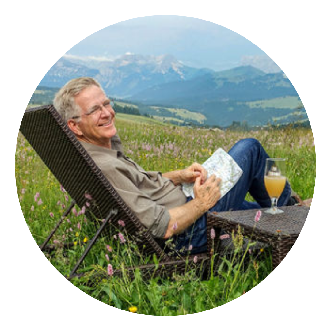 Rick Steves in a chair in a meadow beneath a mountain